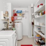 Clean and organized home laundry room with washing machine, shelves, and water heater.