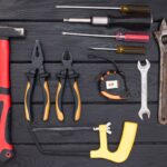 A flat lay photograph of various hand tools on a black wooden surface, ideal for workshops.